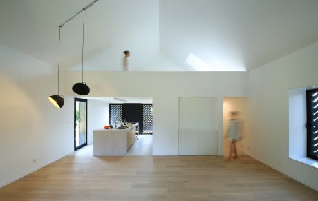 Minimalist open-concept interior with skylights, modern kitchen, and blurred figure in background.