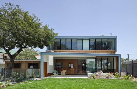 Modern, energy-efficient home with expansive glass walls, wood accents, and lush landscaping.