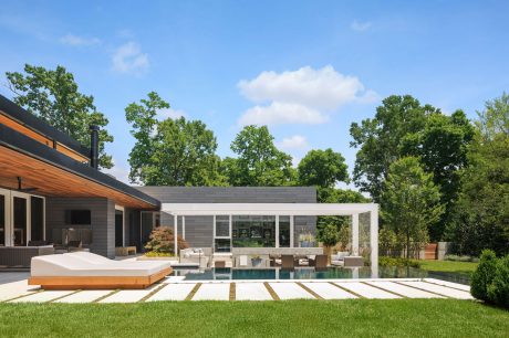 Modern glass-walled poolhouse with sleek rectangular design and lush surrounding trees.