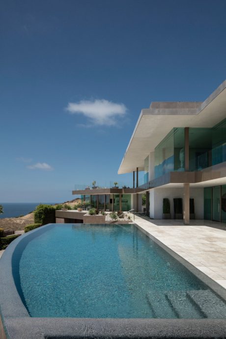 Sleek modern architecture with a stunning pool and lush landscaping overlooking the ocean.