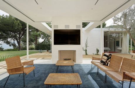 Spacious modern outdoor living area with a fireplace, woven furniture, and large windows.