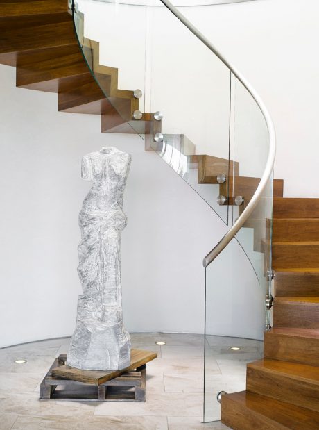 A modern, wooden staircase with glass railings and a large sculptural piece on a platform below.