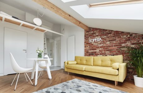 Bright, airy living space with exposed wooden beams, brick wall, and yellow sofa.