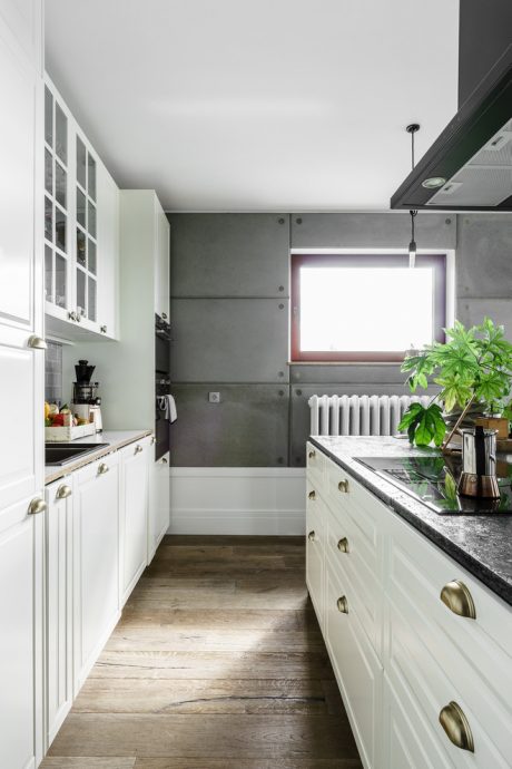 Minimalist kitchen with white cabinets, gray concrete walls, and wood floor.