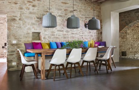 A cozy dining area with rustic stone walls, pendant lights, and a colorful, modern table setting.