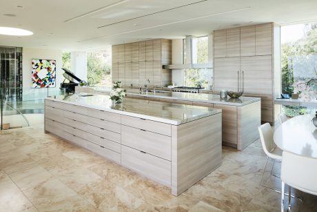 Spacious modern kitchen with sleek wood cabinetry, large island, and natural stone flooring.