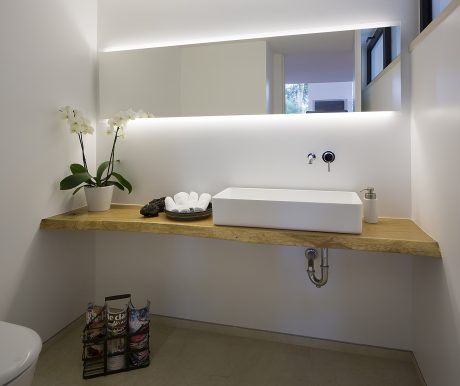 Minimalist bathroom with wood vanity, vessel sink, and illuminated mirror.