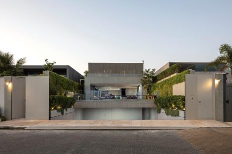 A modern, open-concept residential exterior with lush greenery, clean lines, and glass walls.