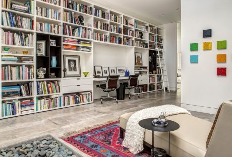 A modern home office with floor-to-ceiling bookshelves, artwork, and colorful decor.