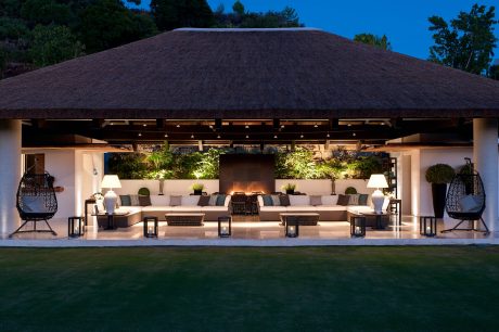 Expansive outdoor lounge with thatched roof, plush seating, lush greenery, and warm lighting.