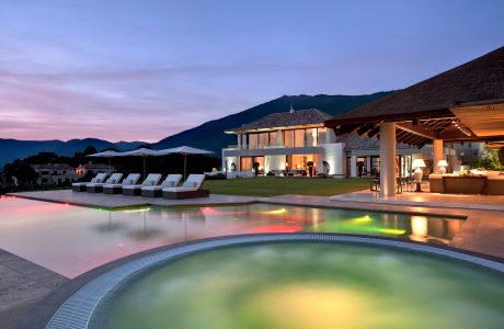 Luxurious villa with modern architecture, illuminated pool, and mountain backdrop.