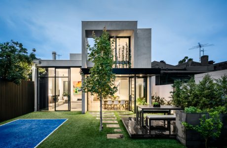 Modern architectural home with glass walls, pool, and lush greenery surrounding the exterior.