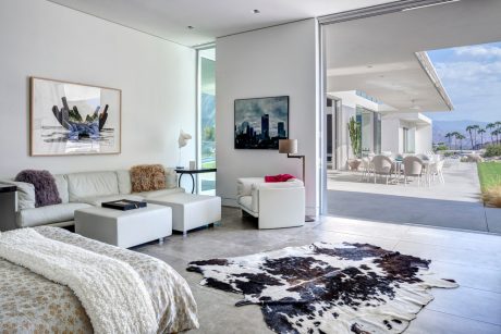 Modern, open-plan living space with large windows, gray sofa, and abstract wall art.