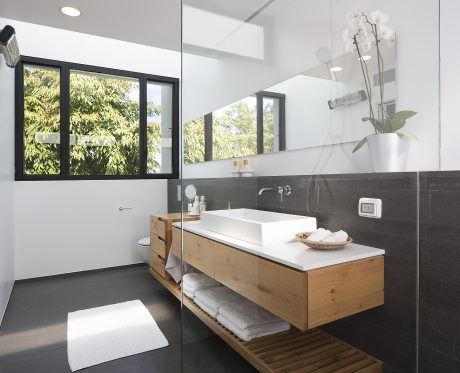 Modern bathroom with black window frames, wooden vanity, and potted orchid.
