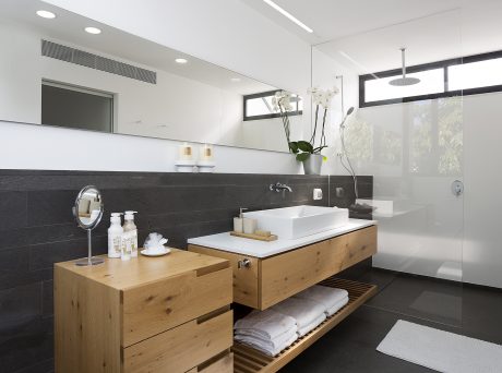 A modern bathroom with black tile walls, a white vessel sink, and a natural wood vanity.