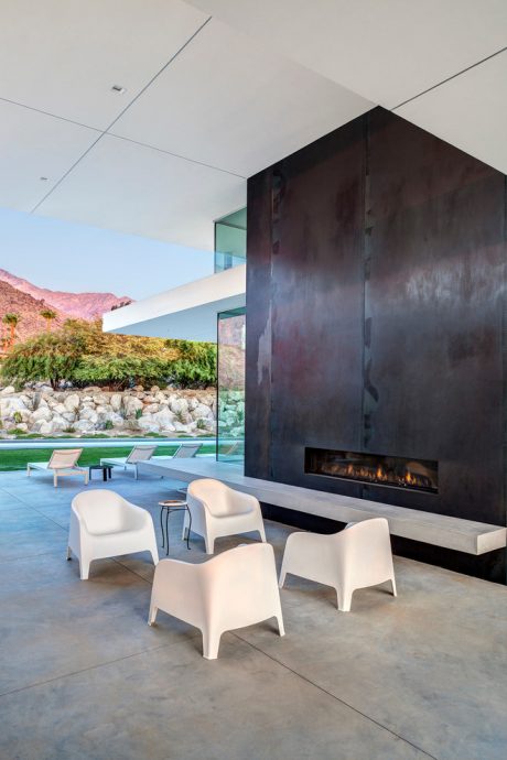 Sleek modern patio with concrete floor, minimalist white chairs, and a large fireplace.