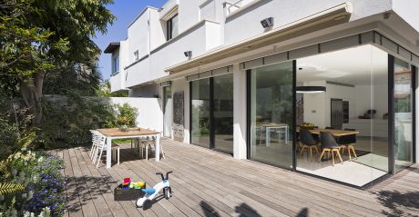 Modern white building with large glass windows, wooden deck, and outdoor dining area.