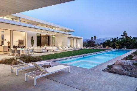 Sleek modern home with large pool, lounging area, and expansive views of mountains.