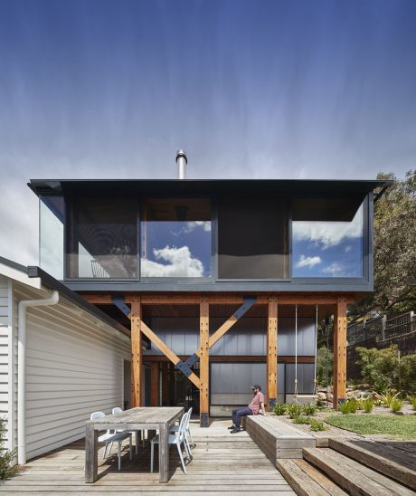 Modern wooden structure with large windows, deck, and outdoor seating area.