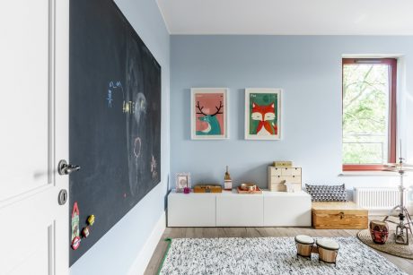 Cozy, modern kids' room with chalkboard wall, framed artwork, storage furniture, and natural light.
