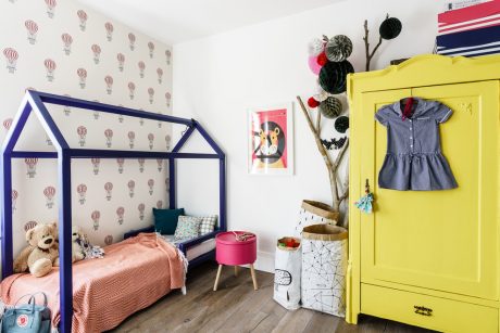 Bright, colorful children's bedroom with patterned walls, a house-shaped bed frame, and a vibrant yellow wardrobe.