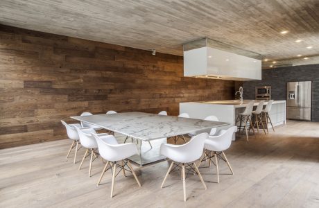 Modern open-concept kitchen and dining area with wooden walls, marble table, and white chairs.