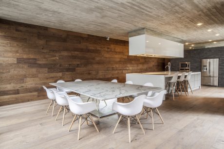 Modern open-concept kitchen and dining area with wooden walls, marble table, and white chairs.