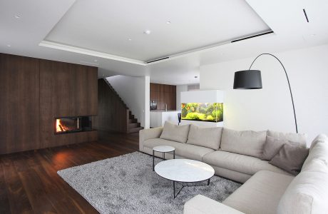 Modern, minimalist living room with wood-paneled walls, fireplace, and gray furniture.