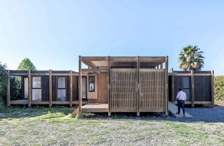 Modern, modular wooden cabin with patio and slat-wood accents, set amidst nature.