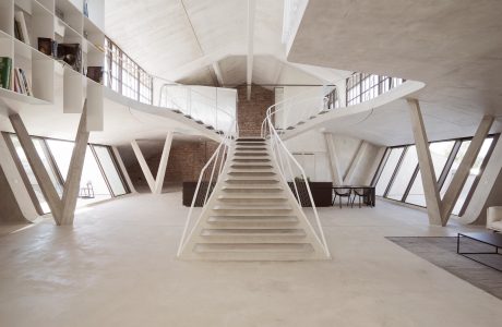 Striking architectural interior with geometric, angular staircase and exposed brick walls.