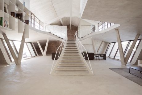 Striking architectural interior with geometric, angular staircase and exposed brick walls.