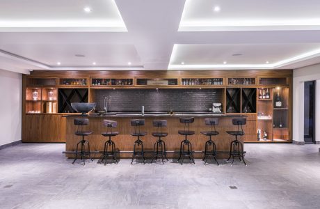 Elegant bar area with wooden paneling, shelving, and stools against a tiled floor and backdrop.