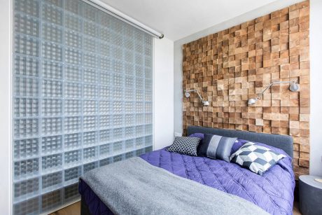 Bedroom with textured wood accent wall, glass block window, and vibrant purple bedding.