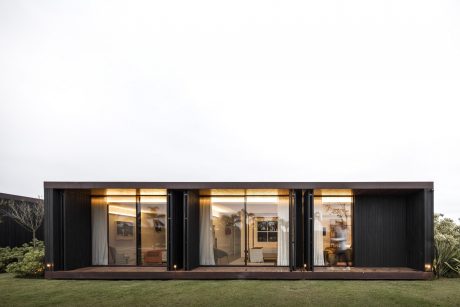 A modern, minimalist home with large glass windows framed by a dark exterior and wooden deck.