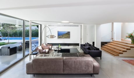 Modern, open-plan living room with large windows, sleek furniture, and wooden staircase.