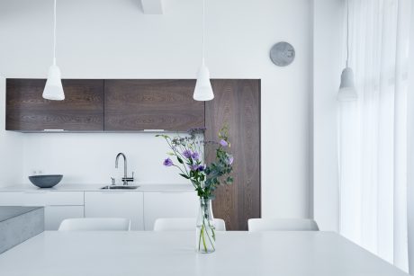 Minimalist kitchen design with contrasting dark wood cabinetry and white walls, accented by a vase of purple flowers.