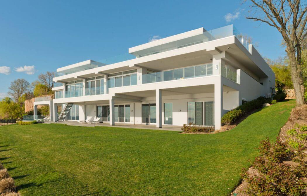 A modern, multi-level building with clean lines, large windows, and a lush green lawn.
