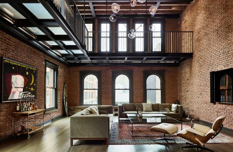 Expansive loft space with exposed brick walls, arched windows, and modern furnishings.