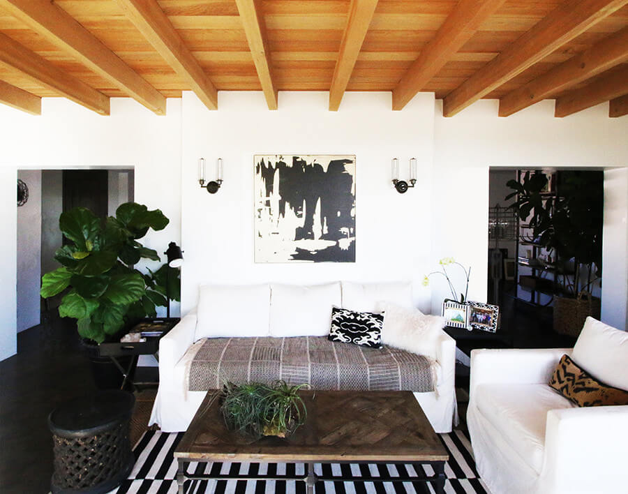 Rustic wooden ceiling beams, minimalist white decor, and patterned textiles create a cozy ambiance.