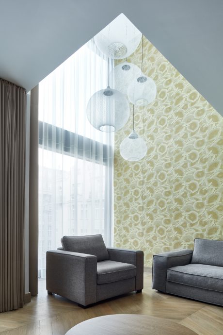 Modern living room with geometric light fixtures, floral wallpaper, and grey furniture.