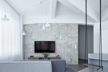 Modern minimalist living space with sleek concrete walls, suspended lighting, and a TV console.