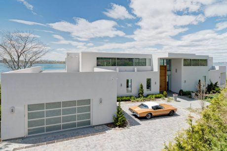 Modern, sleek home with glass walls, private courtyard, and luxury vehicle.