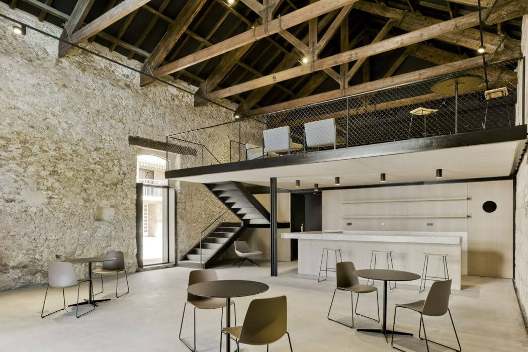 A modern industrial interior with exposed wooden beams, stone walls, and minimalist furnishings.