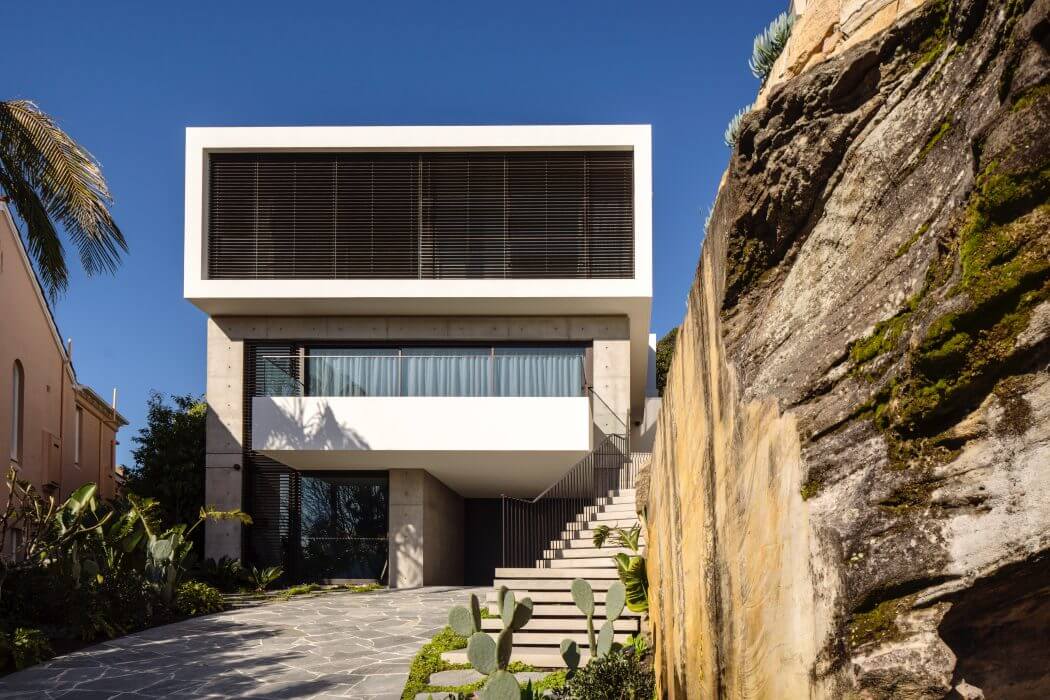Modern cliffside villa with sleek white façade, shaded balcony, and stone retaining wall.