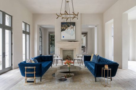Elegant living room with luxurious blue sofas, fireplace, and modern chandelier.