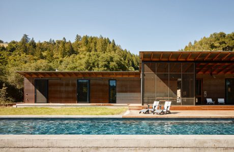 Sleek modern residence with glass walls, wooden beams, and a striking pool surrounded by lush greenery.