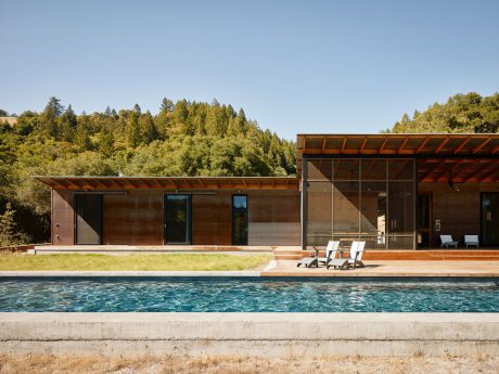 Sleek modern residence with glass walls, wooden beams, and a striking pool surrounded by lush greenery.