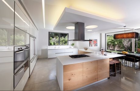 A modern kitchen with sleek white cabinetry, wooden accents, and a large island with a gas cooktop.