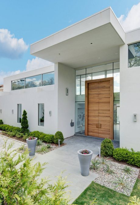 Modern architectural design with wooden entrance door, large windows, and well-landscaped exterior.