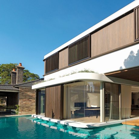 A modern home with a sleek, angular design, featuring a glass wall overlooking a swimming pool.
